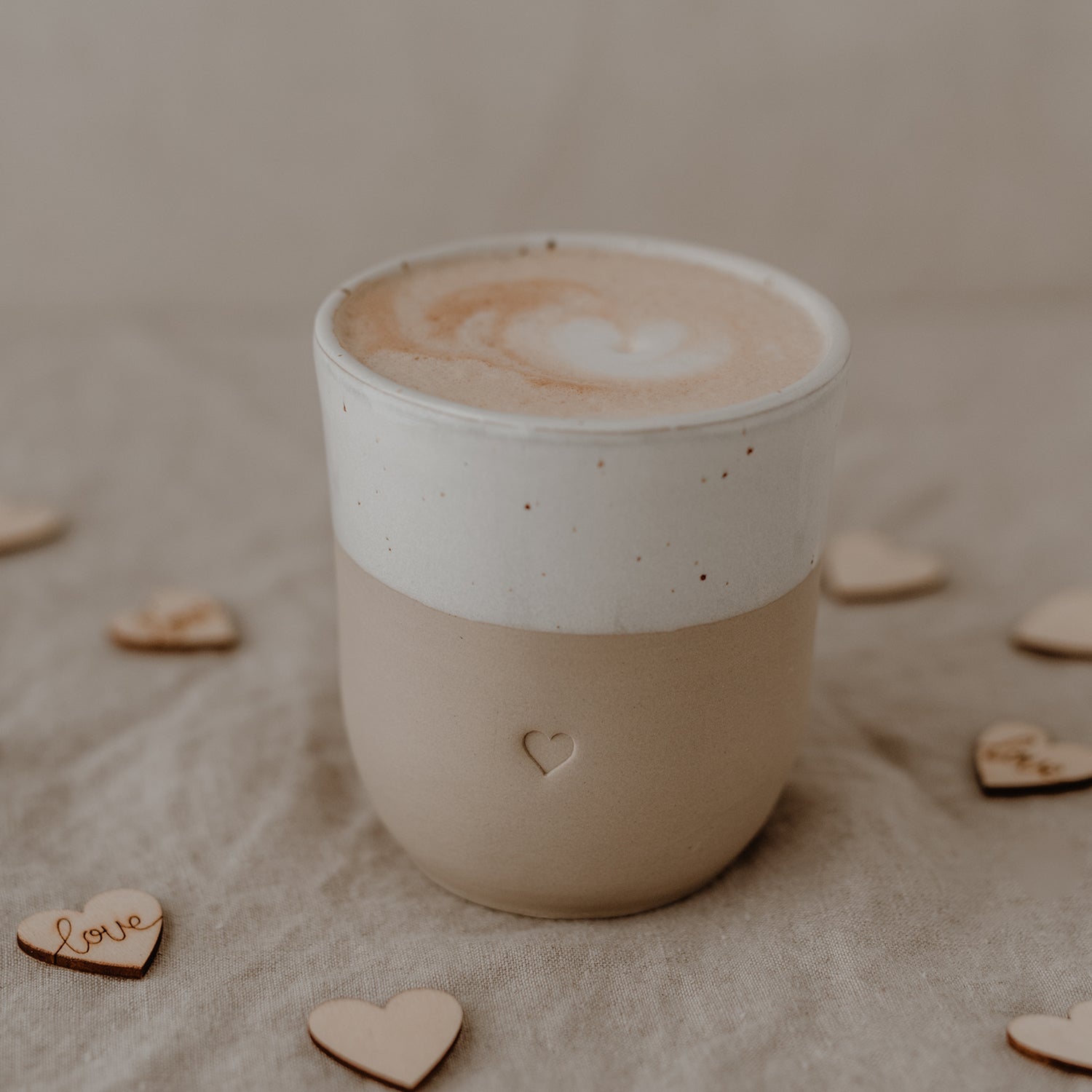 Becher Herz mit Kaffee gefüllt auf Leinedecke und Holzherzen darum gestreut