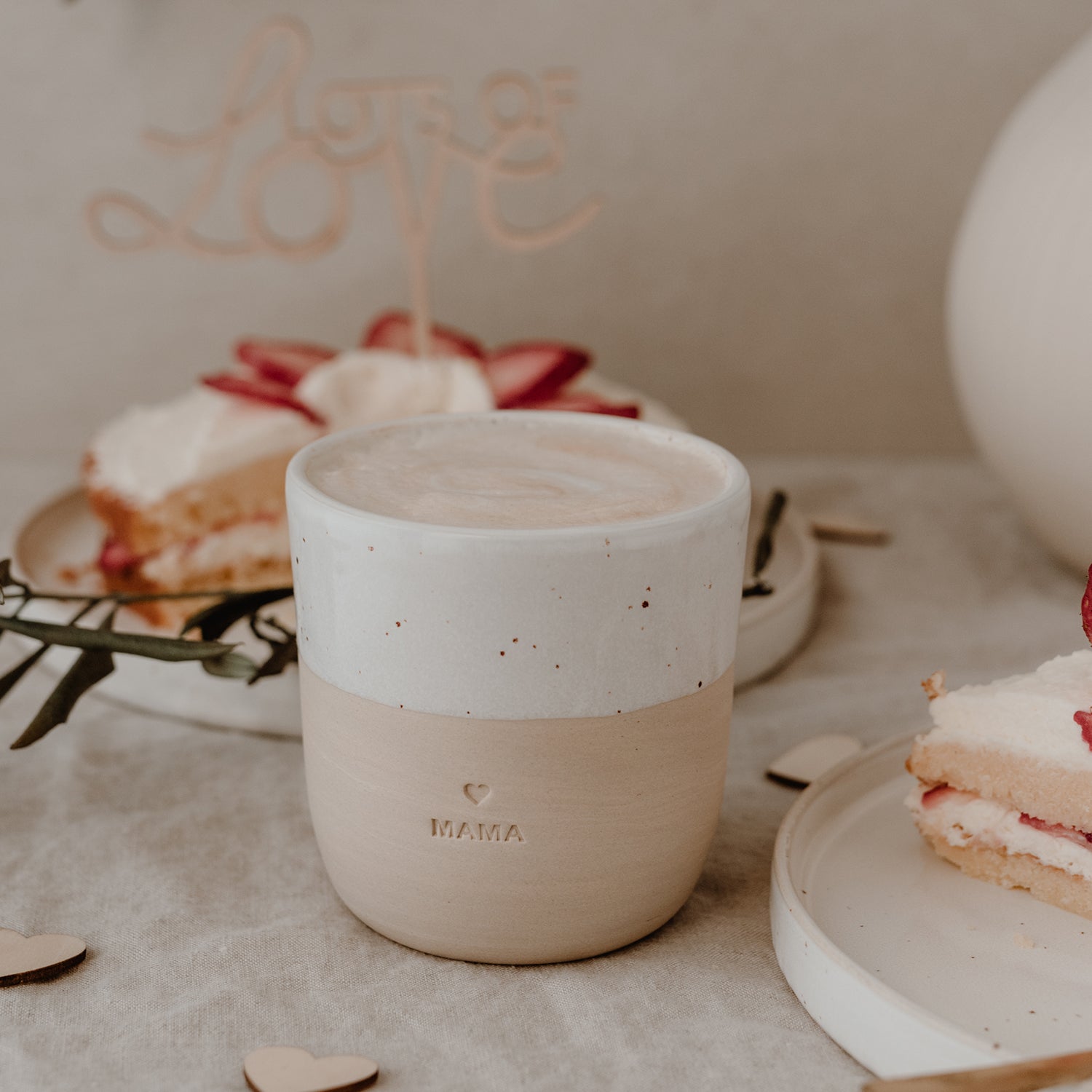 Becher Mama mit Kaffee gefüllt vor Kuchenplatte im Hintergrund